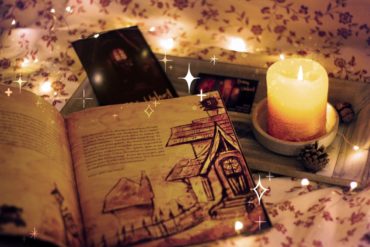 Das Buch Ernas Unheil liegt aufgeschlagen auf einem Tisch. Daneben steht eine Kerze