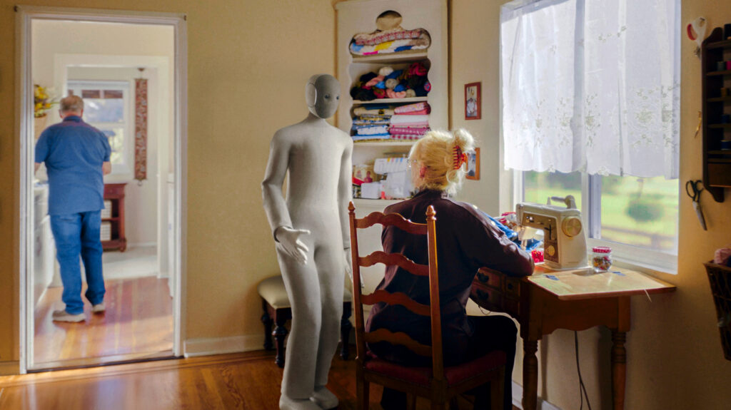 Der NEO Roboter wendet sich einer älteren Dame zu, die an einer Nähmaschine sitzt